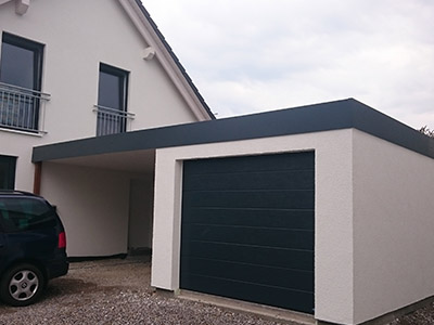 Blick auf eine isolierte Einzelgarage mit zusätzlichem Unterstand gebaut von M.S. Garagenbau GmbH. Hochwertige Bauweise für langlebigen Schutz. Das Bild zeigt eine isolierte Einzelgarage von M.S. Garagenbau GmbH die an ein Einfamilienhaus angeschlossen ist. Zwischen dem Haus und der Garage ist ein zusätzlicher Unterstand für ein Fahrzeug. So erhält man neben einer Garage auch zusätzlichen Stauraum.